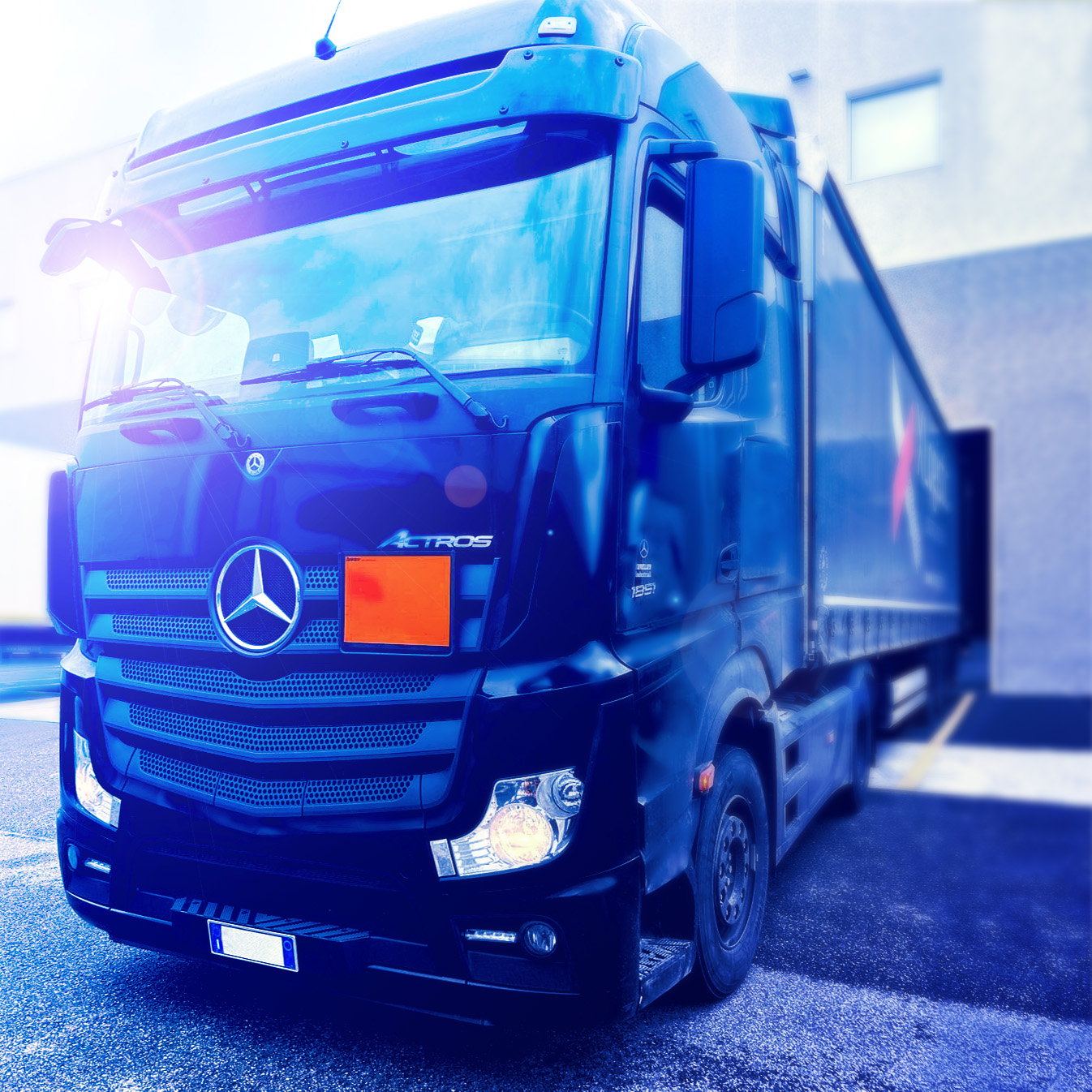 Camion Mercedes per il trasporto di merci pericolose, con targa arancione ADR sulla griglia frontale. Il veicolo è parcheggiato vicino a un magazzino, pronto per il carico o scarico.